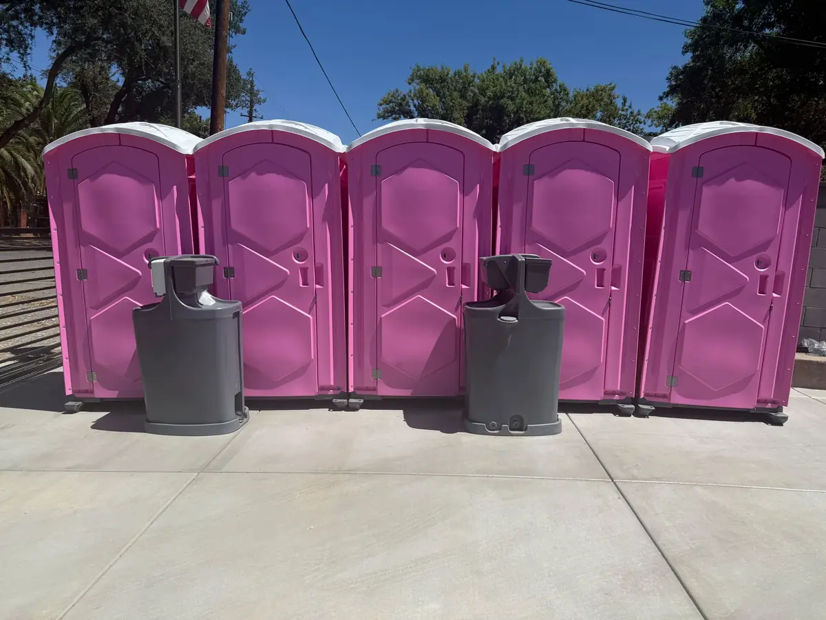 Row of five pink portable toilets with two hand-wash stations on a paved lot